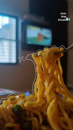 a fork full of noodles on top of a table next to a tv screen with the television in the background