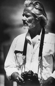 an old black and white photo of a man with long hair holding a camera in his hand