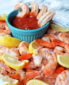 a blue bowl filled with shrimp next to lemon wedges and ketchup on a plate