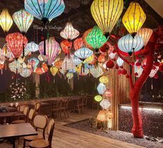 many colorful lanterns hanging from the ceiling above tables and chairs in a room with wood flooring