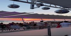 a group of people sitting on top of a boat near the ocean at sunset with disco balls hanging from the ceiling