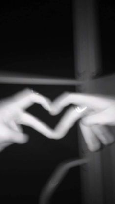 two hands making a heart shape with their fingers in black and white photo taken from below