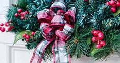 a christmas wreath hanging on the side of a building with red berries and greenery