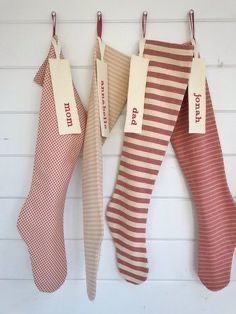 three christmas stockings hanging from hooks on the wall with tags attached to them, one for each stocking