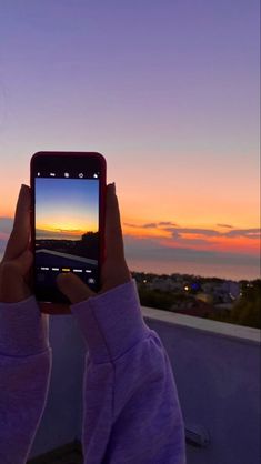 a person holding up a cell phone to take a photo with the sunset in the background