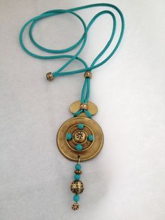 a blue and gold necklace with a bell on the end is laying on a white surface