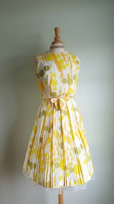 Now that's a cocktail dress! 🍸🍋 This vintage dress looks like an olive martini with a citrus twist, with its fun abstract dot and stem print, bursting with pops of orange, yellow and green on a cream background. It features a blouson-style bodice that buttons in the back; a cinched waist accented by a matching tie sash; and a full, twirly pleated skirt. (Pictured with a crinoline- not included - to demonstrate fullness; its white edge peeks out at the hem.) Bodice is lined; back metal zip at w 1950s Style Summer Cocktail Dress, Yellow Pleated Dress For Cocktail, Yellow Pleated Dress For Cocktail Occasions, Summer Dresses With Box Pleat And Full Skirt, Fitted Pleated Skirt Dress For Garden Party, Fitted Dress With Pleated Skirt For Garden Party, Retro Pleated Summer Dresses, Green Pleated Skirt Dress For Summer, Mid-century Summer Party Dresses