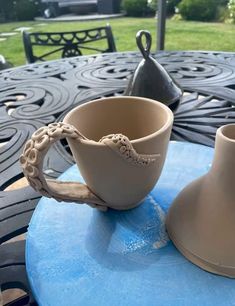 two cups sitting on top of a blue table next to a vase and saucer