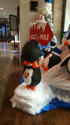 penguins are standing in the middle of an ice rink with fake snow on it and one penguin is wearing a black hat