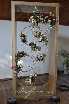 a wooden frame with flowers hanging from it's sides in front of a wall