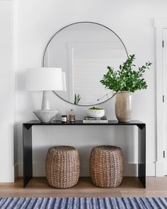 a table with two stools and a round mirror on the wall above it in a white room