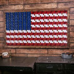 an american flag made out of red, white and blue bottles is hanging on a brick wall