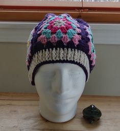 a white mannequin head wearing a multicolored crocheted hat next to a window