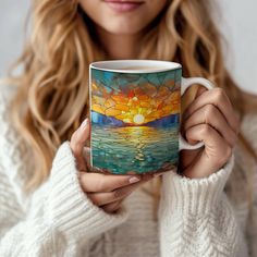 a woman is holding a coffee mug with a sunset painting on the inside of it