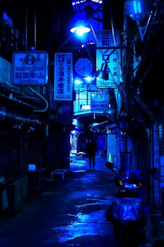 a person walking down a dark alley way at night with neon signs on the buildings