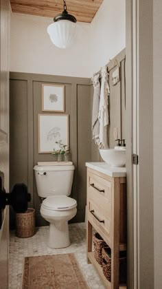 a white toilet sitting in a bathroom next to a sink and wooden cabinet under a light fixture