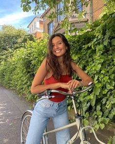 a woman is sitting on her bike in front of some bushes and trees, smiling at the camera