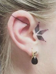 a woman's ear with a small black leaf tattoo on it