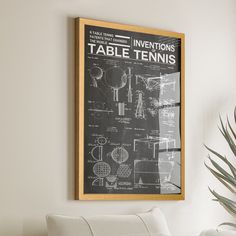 a framed poster on the wall above a white chair and table with a potted plant next to it