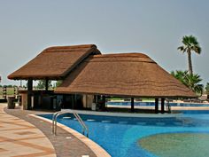 an outdoor swimming pool with thatched roof over it