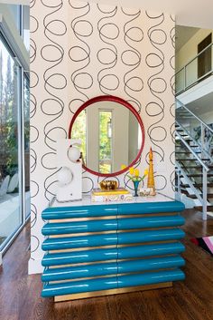 a blue dresser in front of a wall with circles on it and a round mirror