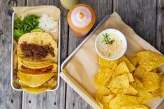 two trays filled with tacos and tortilla chips next to a drink