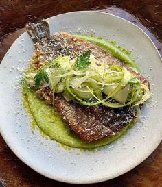 a white plate topped with meat covered in green sauce and garnished with sprouts