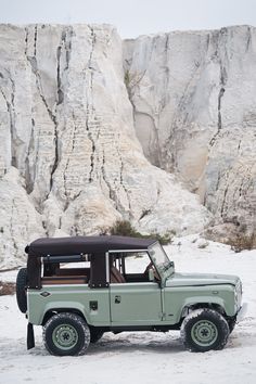 an old green jeep parked in front of a mountain range with snow on the ground