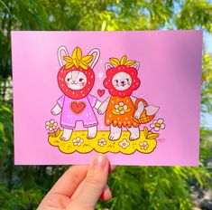 a hand holding up a pink card with two cartoon cats on the front and back