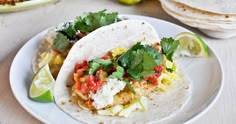 two fish tacos on a plate with limes and tortillas in the background