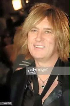 a man with long hair smiling and wearing a black suit at the red carpet event