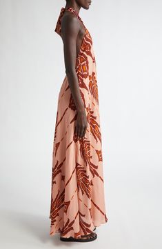 The designer's resortwear roots shine through the breezy silhouette and backless halter design of this embellished silk maxi dress boasting an earthy ikat-inspired print. Halter neck Sleeveless, with cutaway shoulders 100% silk Dry clean Made in Colombia Designer Clothing Hispanic & Latinx Owned/Founded Summer Vacation Silk Halter Dress, Silk Halter Neck Dress For Vacation, Chic Orange Backless Maxi Dress, Silk Halter Dress For Summer Beach, Orange Halter Neck Maxi Dress Beachwear, Silk Backless Maxi Dress For Beach, Backless Silk Maxi Dress For Beach, Orange Maxi Length Halter Dress For Beach, Orange Halter Neck Maxi Dress For Evening