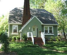 a green house with white trim on the front door and stairs leading up to it