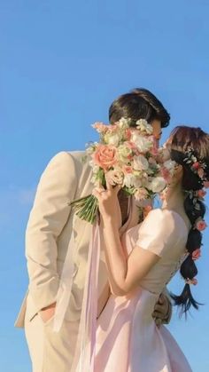 a bride and groom kissing in front of a blue sky with flowers on their heads