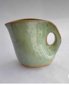 a small green vase with a hole in the middle on a white surface, it appears to be empty