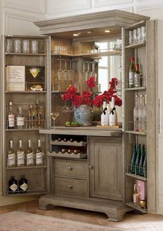 a bar with wine glasses, bottles and flowers on it in a room that has white walls