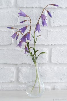 purple flowers in a clear vase against a white brick wall