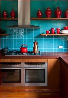 a kitchen with blue tiles and wooden shelves, tea kettles on the stove top