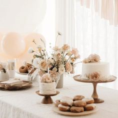 a table topped with cakes and donuts covered in frosting next to white balloons