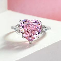 a pink heart shaped diamond ring on top of a white surface