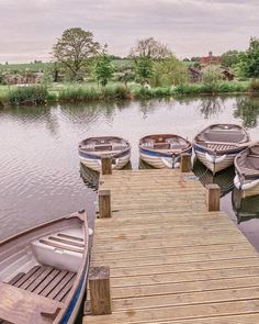 several boats are docked at the end of a wooden dock on a lake with grass and trees in the background