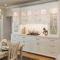 a dining room table and chairs with white cupboards in the center, along with an area rug on the floor