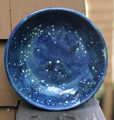 a blue bowl sitting on top of a wooden post next to a building with the sky painted on it