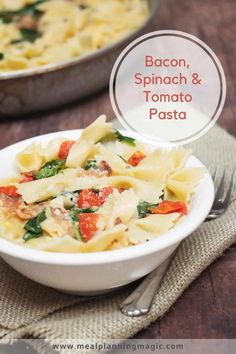 bacon, spinach and tomato pasta in a white bowl with a fork next to it