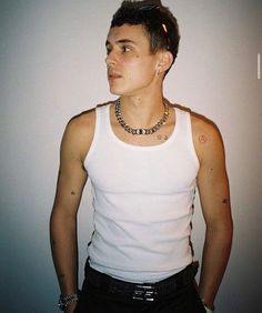 a young man wearing a white tank top and black pants with his hands in his pockets