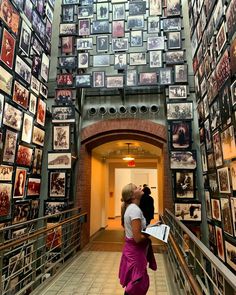 two people walking down a long hallway with many pictures on the walls