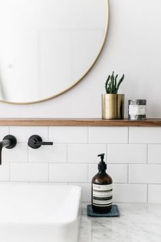 a white sink sitting under a bathroom mirror next to a wooden shelf with soap dispensers on it