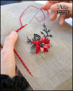 someone is working on an embroidered piece of fabric with red thread and flowers in the center