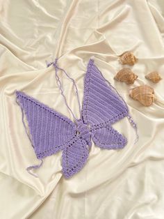 a crocheted butterfly and three seashells laying on a white bed sheet