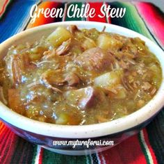 a white bowl filled with green chile stew on top of a colorful table cloth next to a spoon